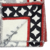 Close-up of a Swedish wool blanket featuring black, white, and red geometric patterns with zigzag stitching along the edges.