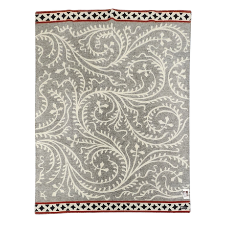 Gray and white wool blanket featuring swirling vine patterns, finished with a geometric border in black, white, and red.