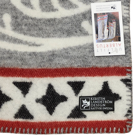 Close-up of a Swedish wool blanket featuring black stars, red and gray stripes, a stitched edge, and two labels, one marked Kerstin Landström Design.