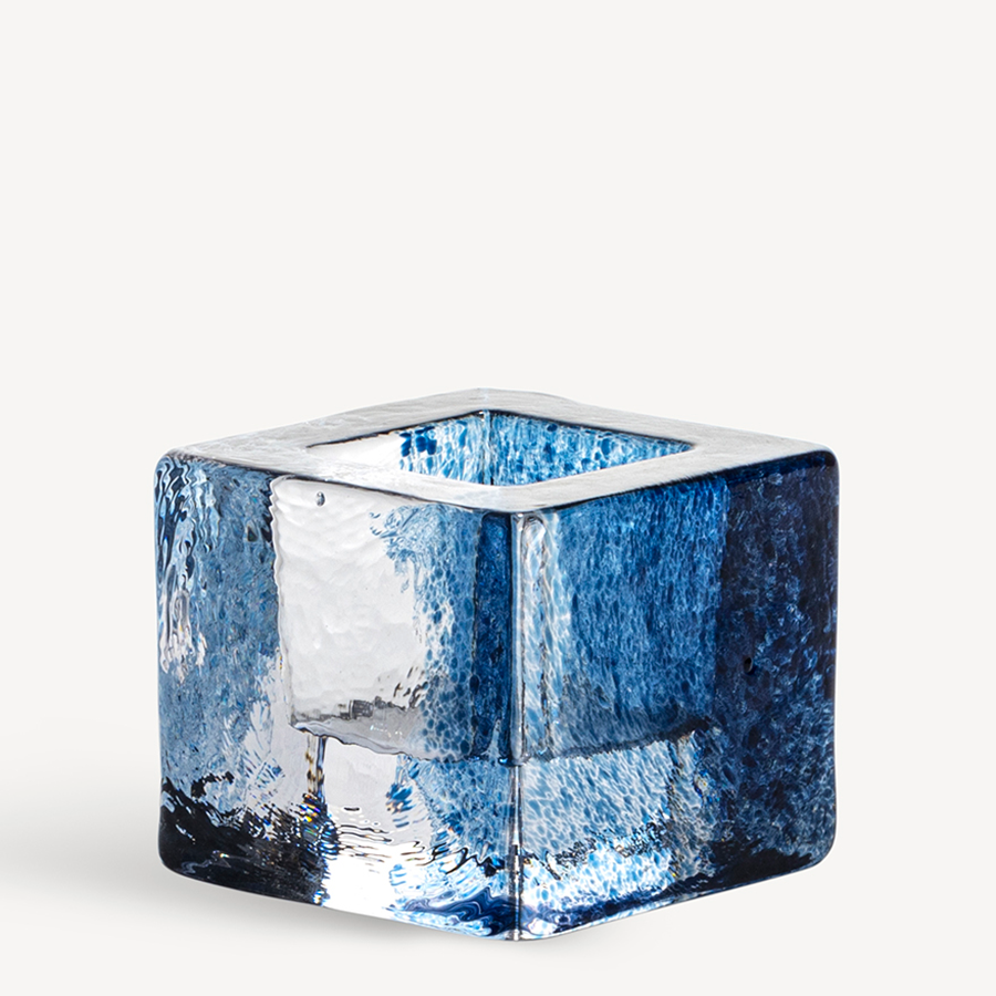 A KostaBoda: Brick Votive Candle Holder, featuring a blue glass cube with a hollow center and textured surface reminiscent of an Anna Ehrner design, rests elegantly against a white background.