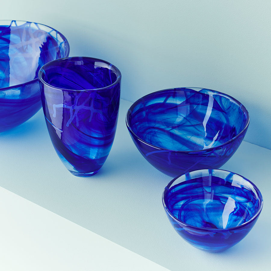 Four KostaBoda: Contrast Bowl Blue Small, designed by Anna Ehrner, elegantly grouped on a light surface capture the Kingdom of Crystals essence with vibrant blues contrasting a soft backdrop.