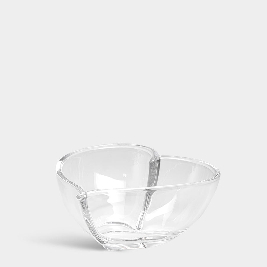 The Orrefors Heart Bowl Large boasts a transparent, smooth finish and divided interior, combining elegance and functionality. This decorative piece is beautifully highlighted against a plain backdrop, making it ideal for any setting.