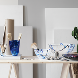 Art supplies and a large KostaBoda Contrast Blue Bowl enhance the wooden table. Paintbrushes are in a blue vase alongside a paper roll and small cactus, forming an inspiring creative workspace.