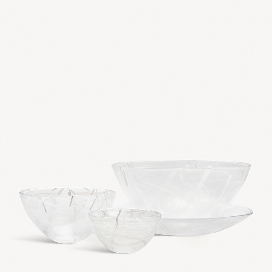 A set of four transparent KostaBoda: Contrast Bowl White and one plate, each varying in size, elegantly arranged on a plain white surface. This exquisite ensemble echoes Anna Ehrners artistry for Kosta Boda, adding sophistication—ideal for those who appreciate subtle contrast.