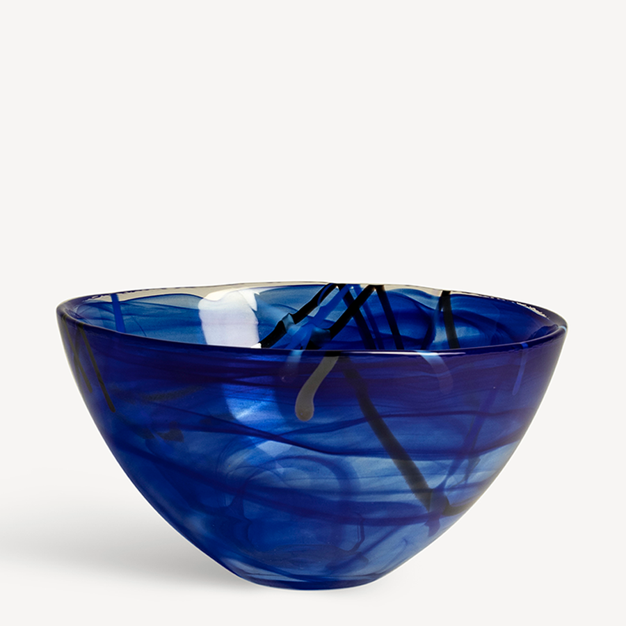 The KostaBoda: Contrast Blue Bowl Medium showcases Anna Ehrners artistic touch with a striking blue glass design and abstract black and yellow patterns on a white background.