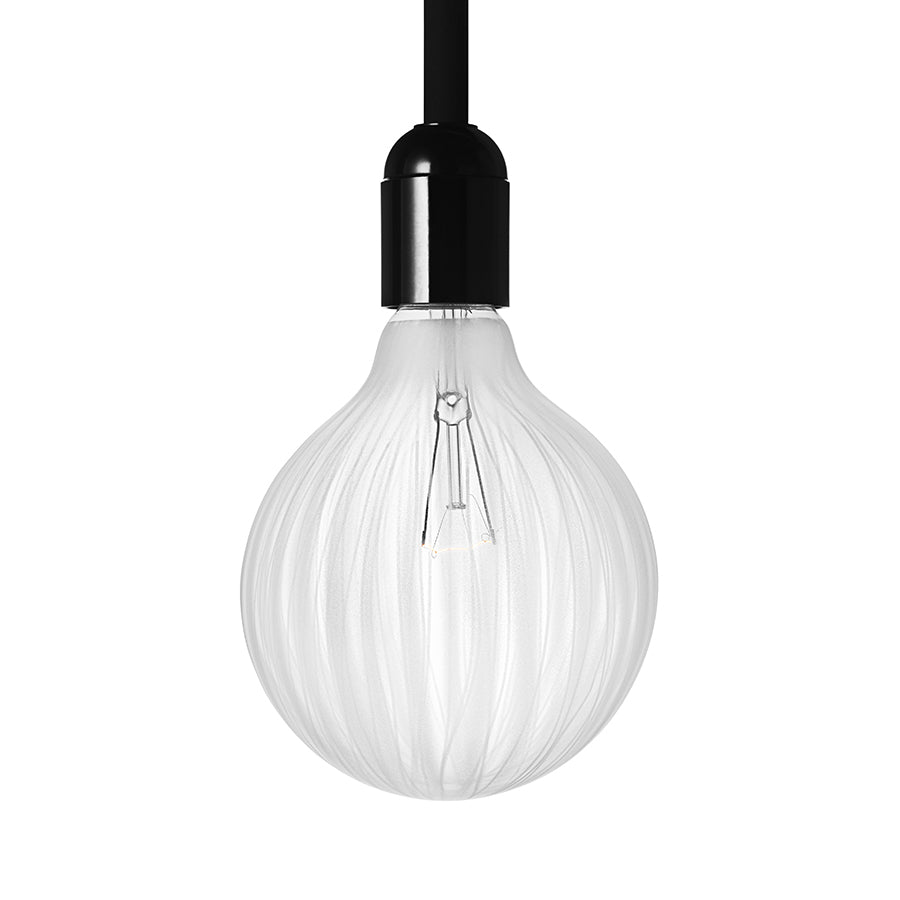 The Orrefors Light Shadows Bulb Cocoon 25W hangs from a sleek black fixture, showcasing minimalist design with its spherical, textured form against a plain white background.