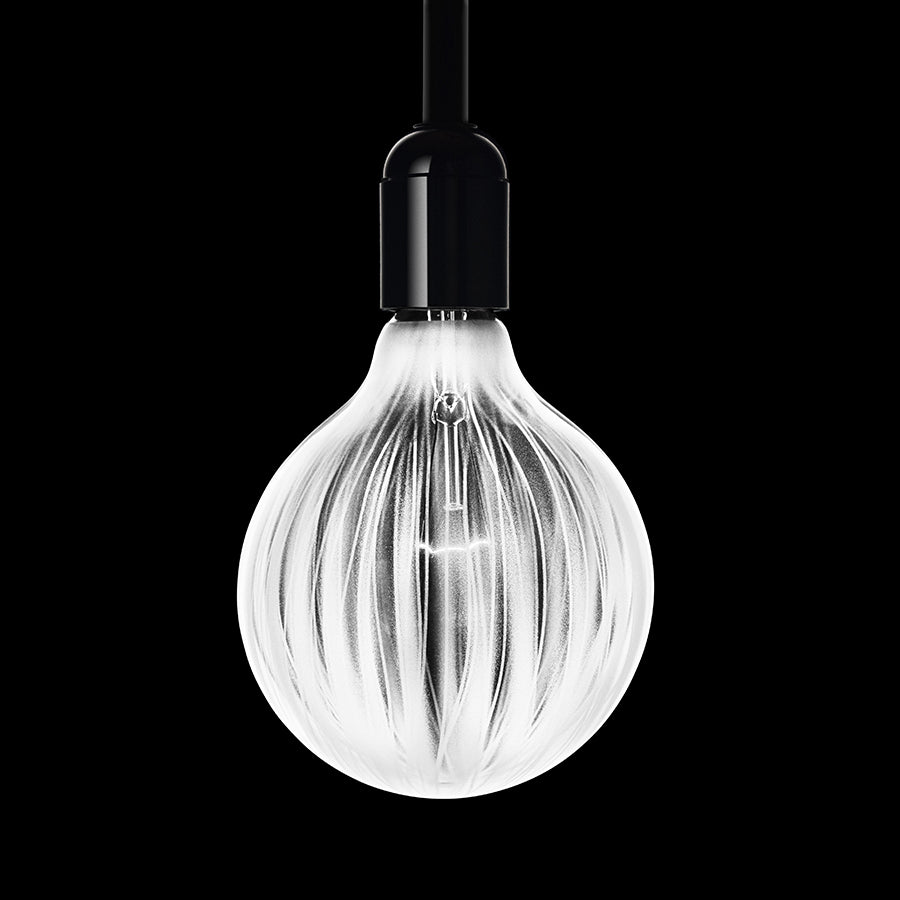 The Orrefors Light Shadows Bulb Cocoon 25W Lightbulb features a glowing, textured design with vertical ridges, elegantly suspended against a black background like a minimalist pendulum lamp.