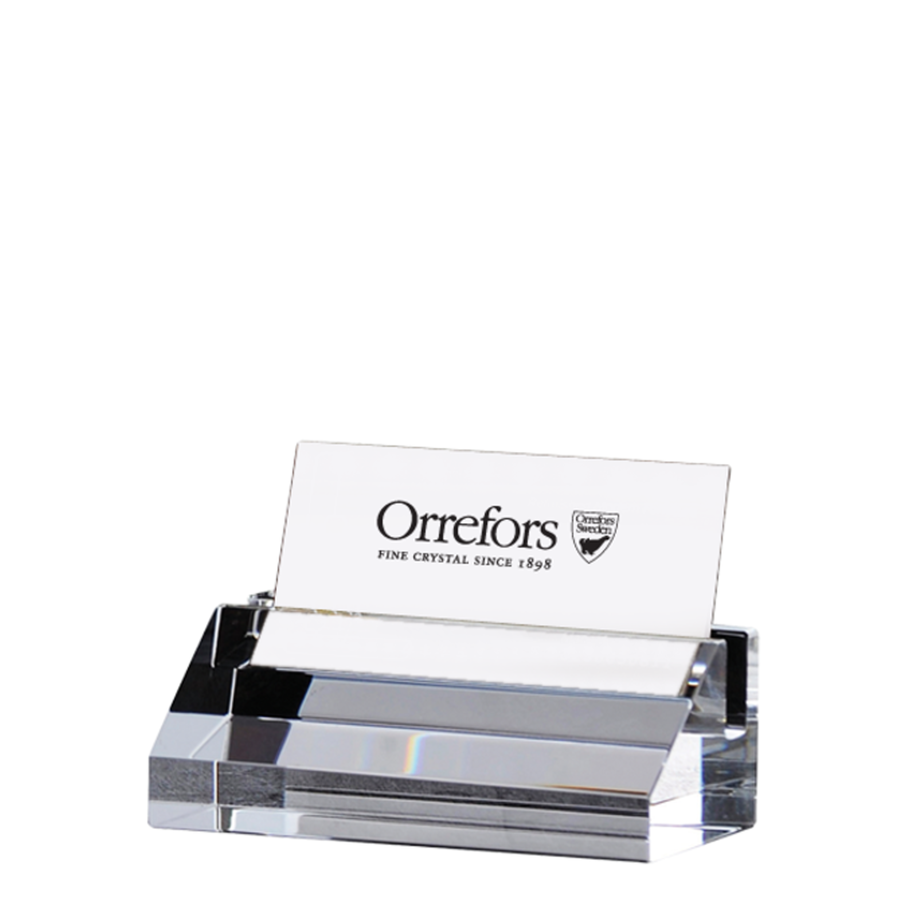 The Orrefors Wall Street Card Holder showcases a minimalist design, crafted from thick crystal. It elegantly holds a single card reading “Orrefors Fine Crystal Since 1898,” reflecting its timeless sophistication.