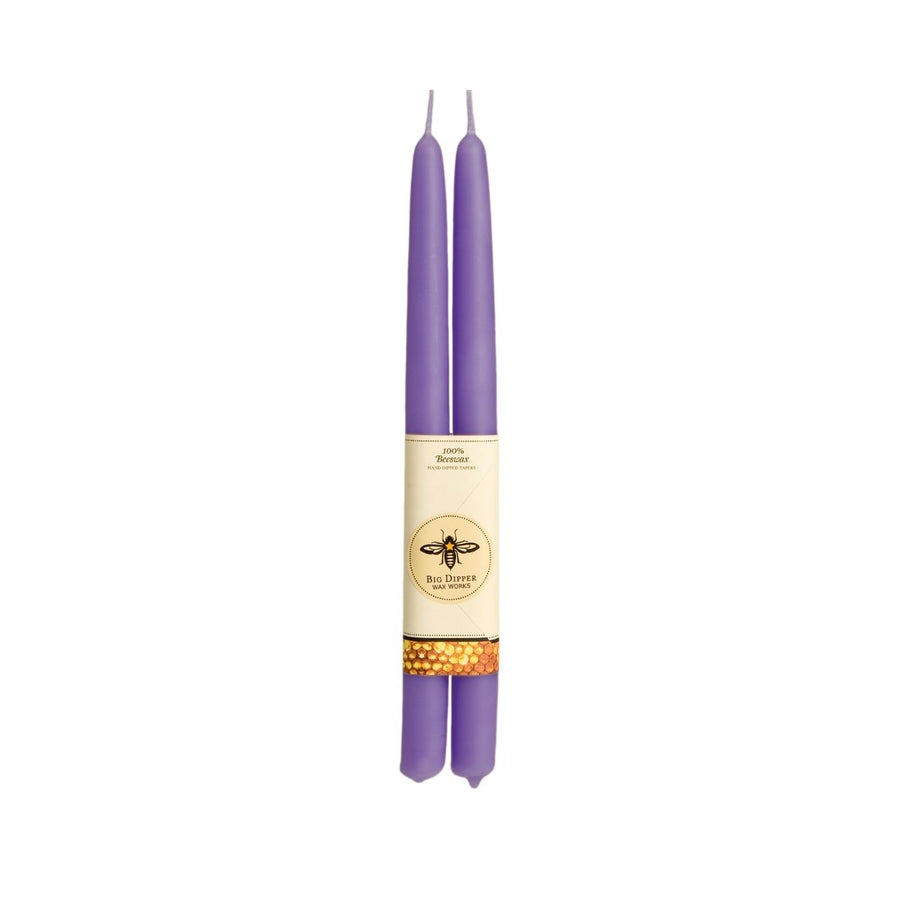 The Big Dipper Wax Works 100% Beeswax Taper Candle Pair features two elegant purple candles, each adorned with a bee emblem and honeycomb design, beautifully hand-crafted and bound by a paper sleeve.