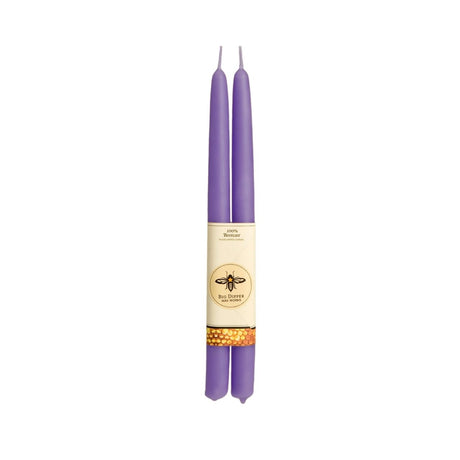 The Big Dipper Wax Works 100% Beeswax Taper Candle Pair features two elegant purple candles, each adorned with a bee emblem and honeycomb design, beautifully hand-crafted and bound by a paper sleeve.