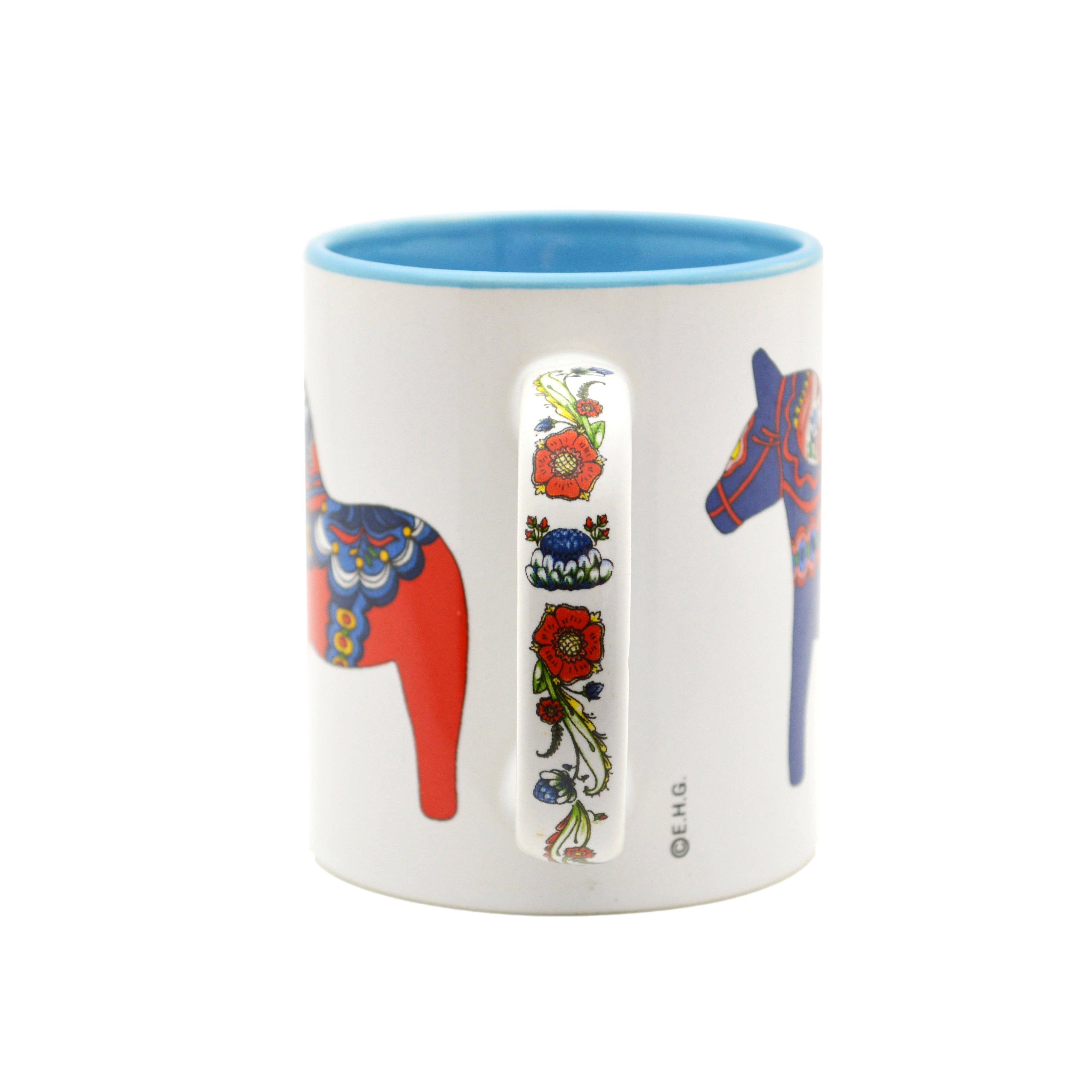 White ceramic coffee mug with a blue interior, featuring a red Dala Horse and vertical floral pattern, inspired by Swedish folk art.