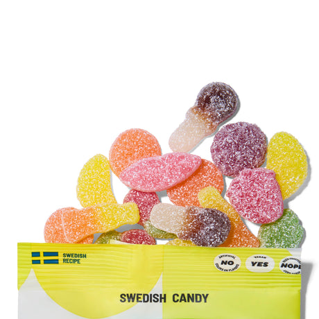 A yellow and white Sockerbit Sour Gummy Mix Swedish Candy Bag 2.8oz spills out colorful, sugar-coated treats. The bag shows “Vegan: YES,” “No Artificial Anything: YES,” and “Non-GMO Ingredients” checkboxes on the front.