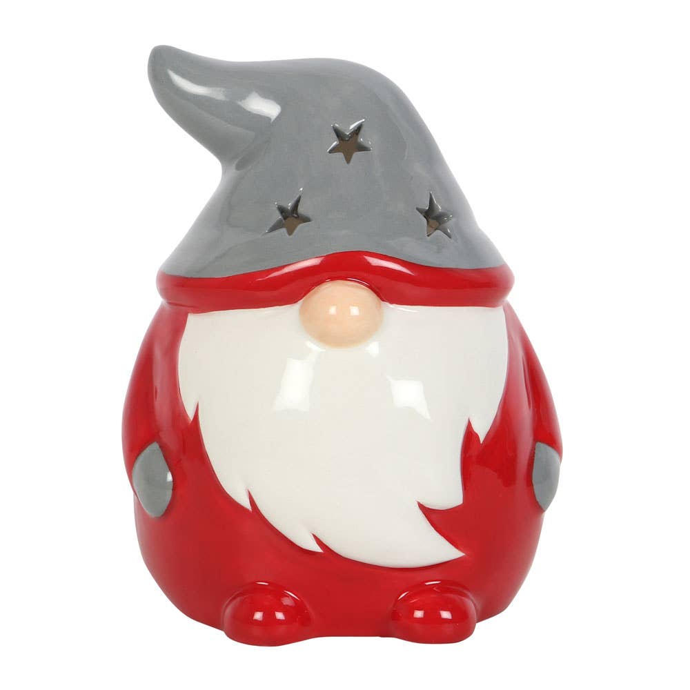 This delightful Candle Holder: Gnome Tealight Holder boasts a gray hat with star-shaped cutouts, a white beard, and a red body. It's ideal for introducing festive cheer and serves as a tealight holder, casting a cozy glow that heightens its holiday appeal.