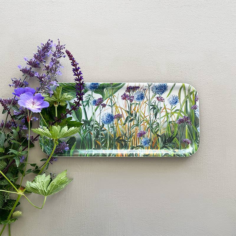 The Anne Just birch veneer tray by Koustrupco, featuring beautiful blue and purple flowers, sits on a light surface surrounded by purple and green flora.