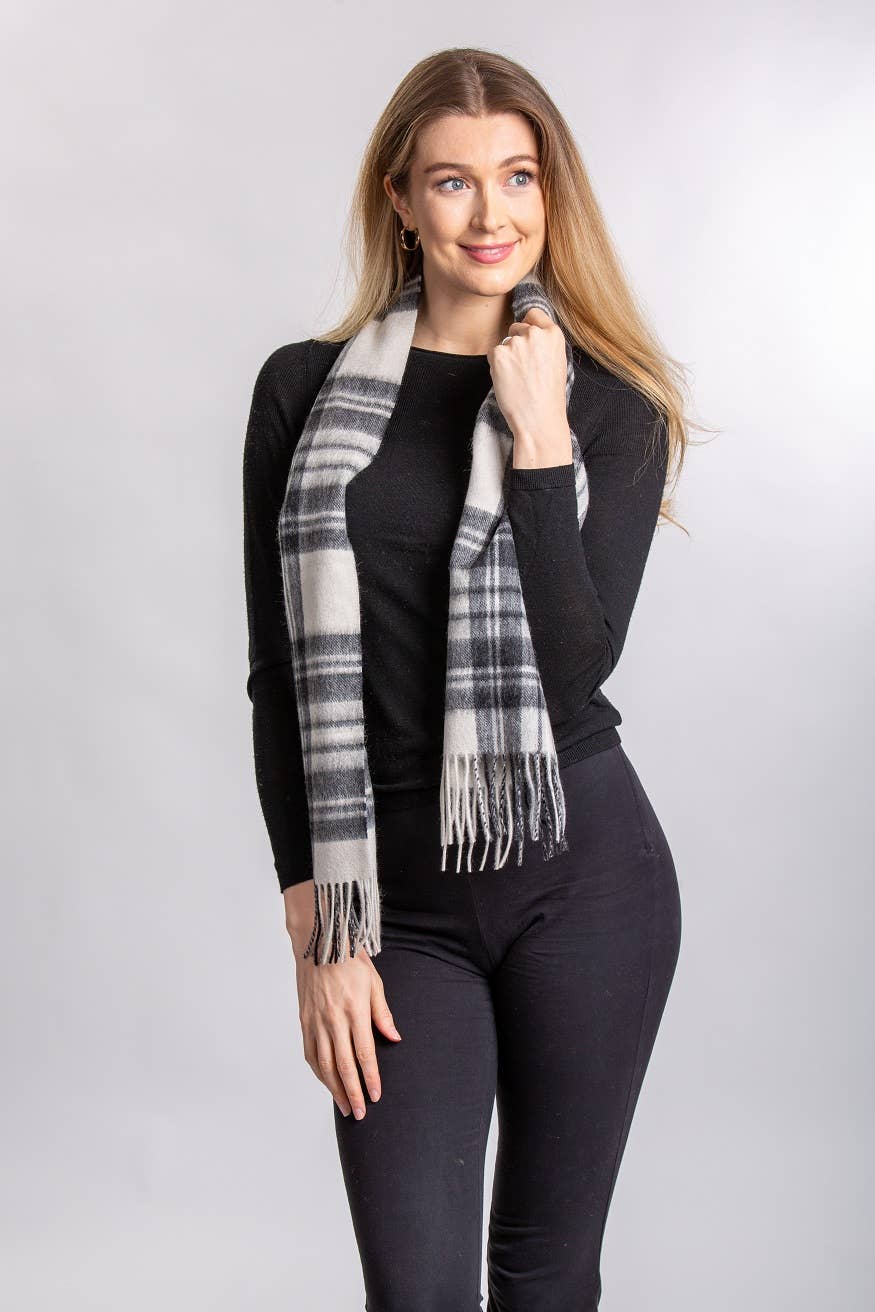 A woman in a black long-sleeve top, black pants, and a Stewart Grey Dress Lambswool Scarf stands against a plain light background.