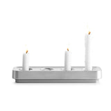 Three white candles, two short and one tall, are lit and elegantly placed in the sleek Stumpastaken Swedish Candle Holder, crafted from recycled aluminum with rounded edges.