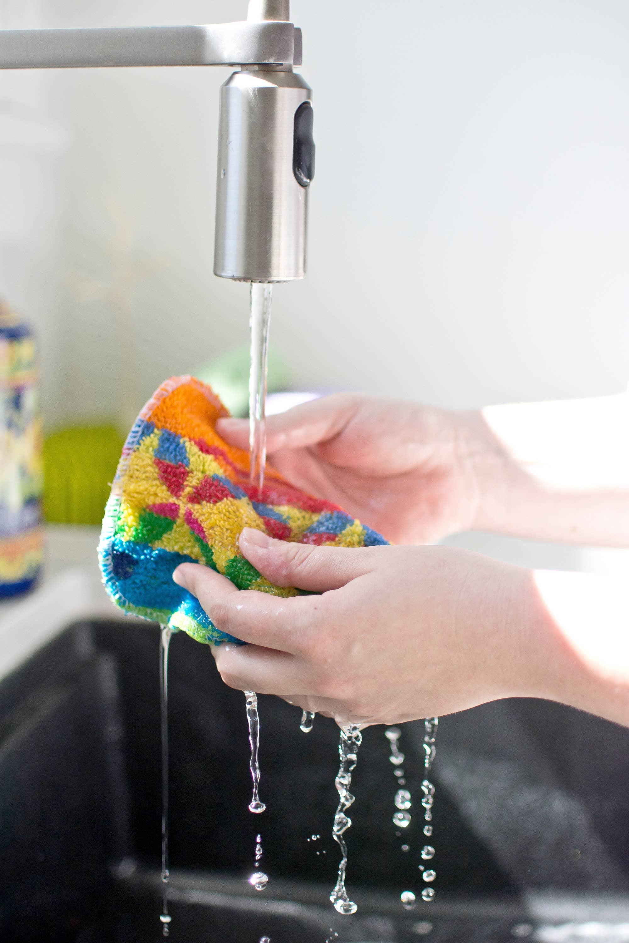 Hands washing a vibrant and eco-friendly Scrub Cloth: Euroscrubby Multi-Purpose Scrubber under a running faucet in a kitchen sink.