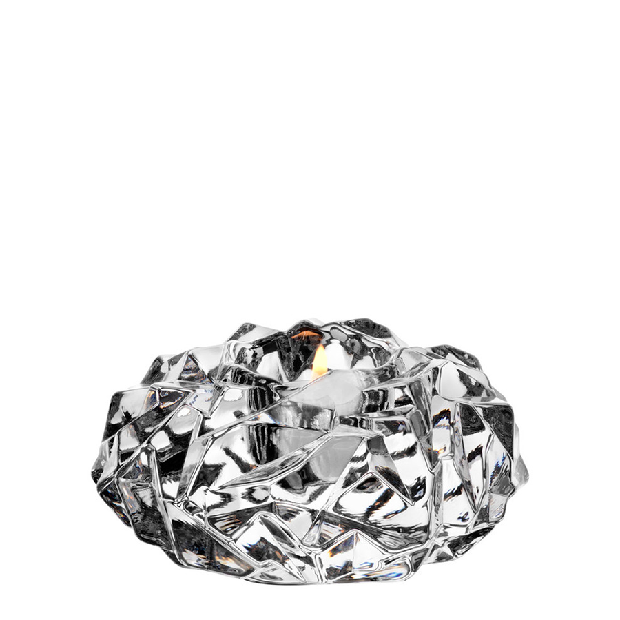 A burning tealight sits in a faceted, crystal-like glass holder set against a white background.