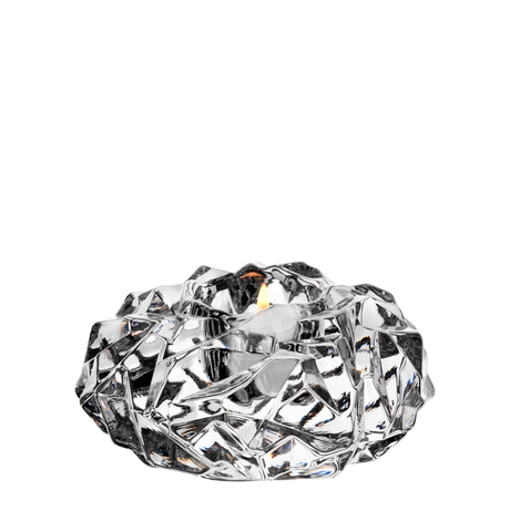 A burning tealight sits in a faceted, crystal-like glass holder set against a white background.