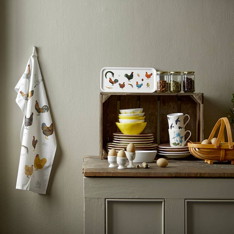 In a delightful kitchen scene, there's a wooden crate with dishes, a Chicken birch veneer serving tray (32x15) showcasing Danish design, and a tea towel adorning the wall. Nearby, eggs are placed on the counter next to an eco-friendly Nordic birch veneer basket. This combination of rustic charm and Scandinavian style is truly inviting.