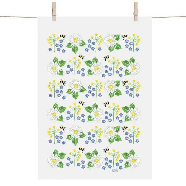 The Swedish Summer Flowers Tea Towel by Anneko Design Sweden hangs on a line, adorned with daisies, yellow and blue blooms, green leaves, and small bees in a vibrant floral pattern.