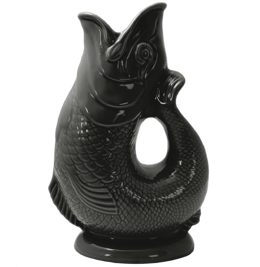 The Gluggle Jug: Black Fish Shaped Pitcher that Gluggles features detailed scales, an open mouth, and a handle formed by the fish’s curved tail in glossy black ceramic.