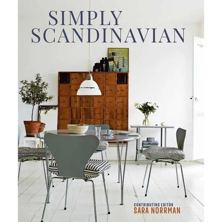 Cover of Simply Scandinavian by Sara Norman features a minimalist room with a dining table, chairs, plants, and a wooden cabinet made from natural materials, epitomizing Scandinavian interior design.