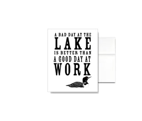 The A Bad Day at the Lake is Better than a Good Day at Work Card features linen texture, lake-inspired text, and a loon illustration—perfect for lakehouse stationery fans and as a thoughtful greeting card.