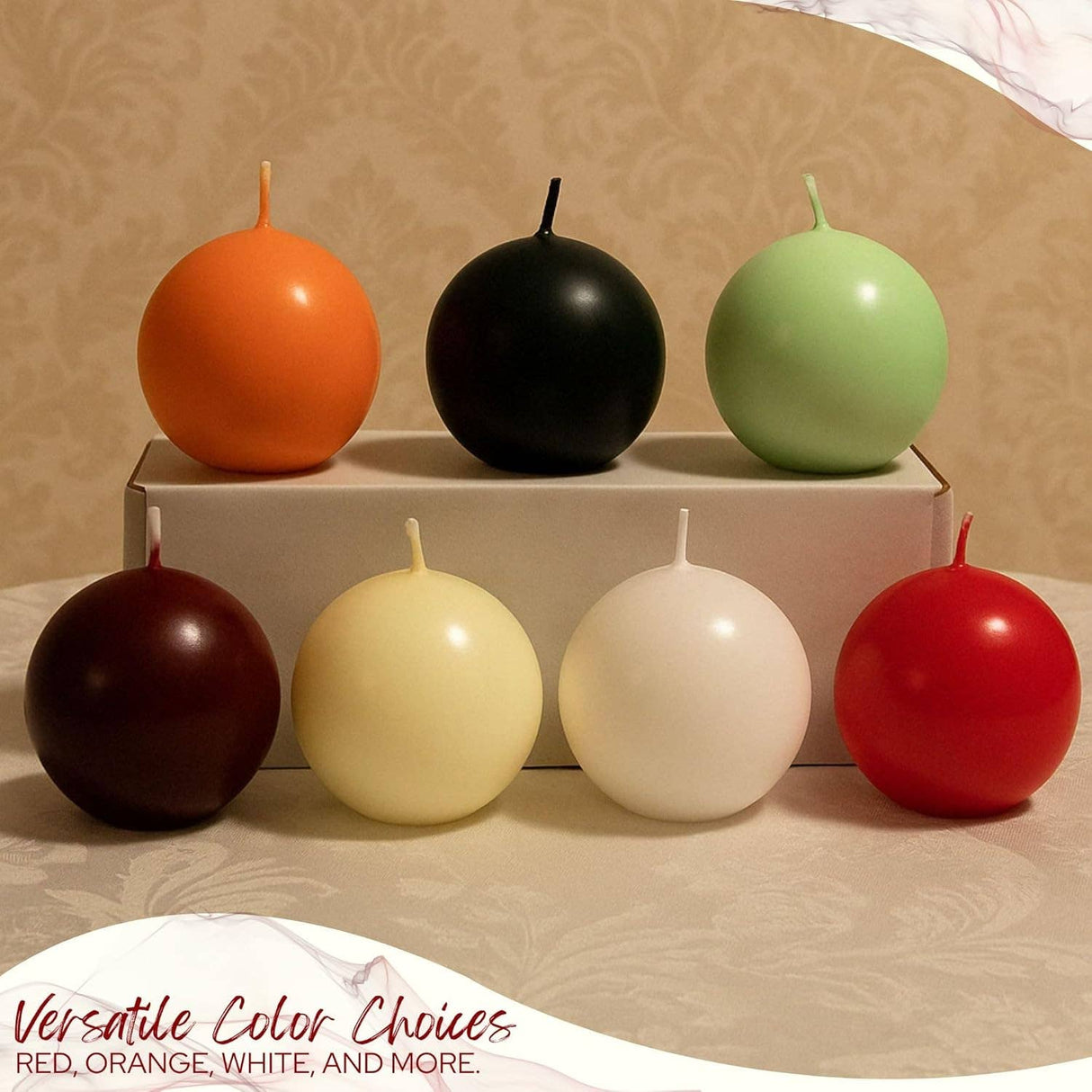 A set of decorative candles, including 2.5" white ball candles, are displayed with orange, black, green, brown, cream, and red candles on and in front of a white box atop a beige patterned tablecloth.