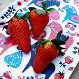 Three large strawberries with green leaves rest on the Swedish Dala Horse Birch-Wood Tray (8x10.5"), decorated with colorful, stylized animal and plant motifs.