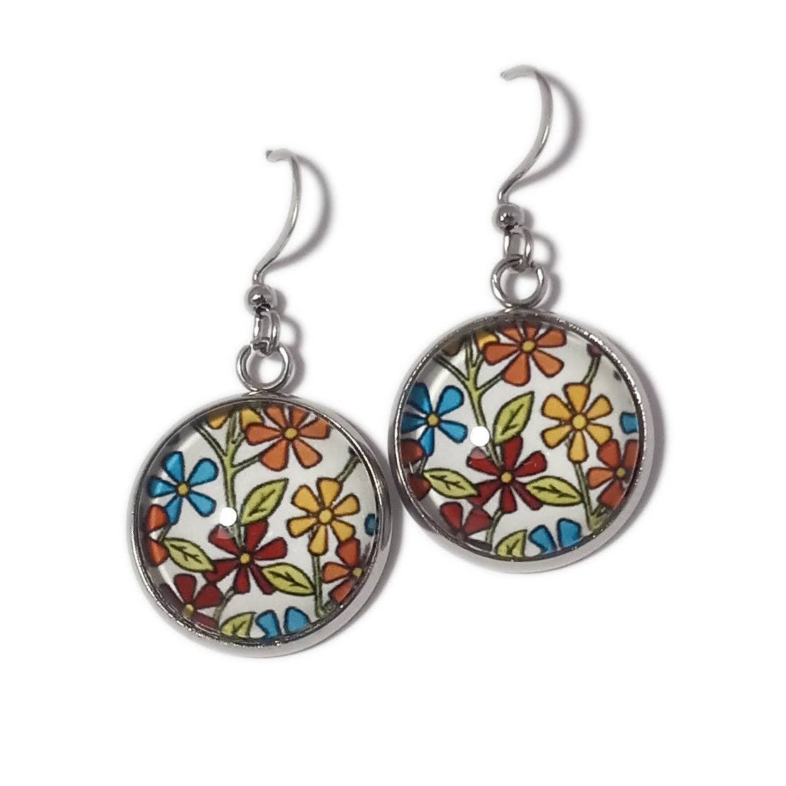 The "Earrings: Flowers on White by Sarah Angst" are handmade and feature a vibrant floral pattern in shades of blue, red, yellow, and green. These earrings are set in a silver frame with hooks, evoking the appearance of mini giclee prints.