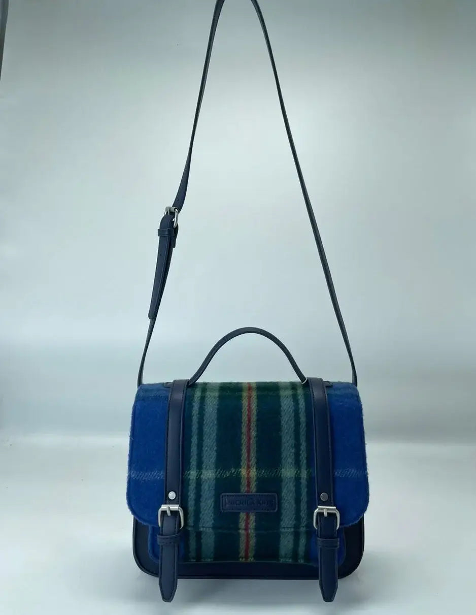 The Bag: Nova Scotia Patsy Handbag is a satchel-style accessory with blue, green, and red Provincial tartan fabric on the front, blue leather trim, adjustable shoulder strap, top handle, and buckle closures.