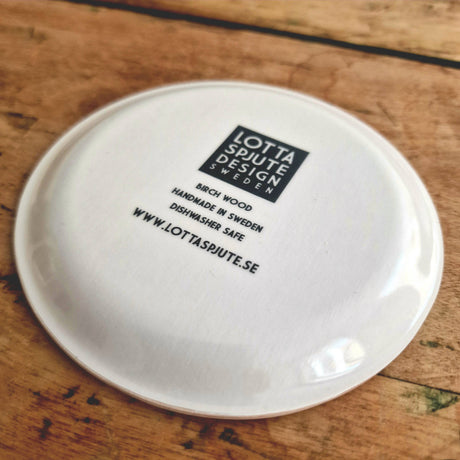 The bottom of the Swedish Dala Horse Birchwood Coaster by Lotta Spjute Sweden displays the logo, material details, and website in black text—a charming detail echoing Swedish design.