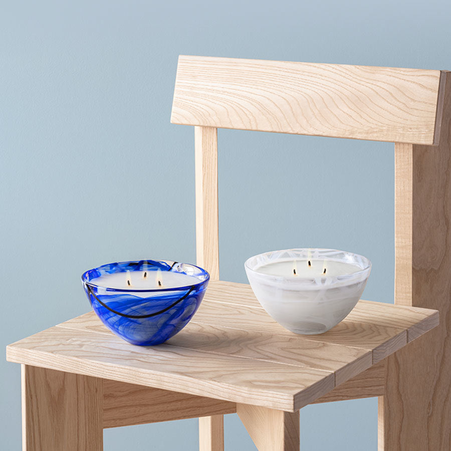 Two KostaBoda: Contrast Candle Blue candles sit gracefully on a wooden chair, set against a serene light blue background.