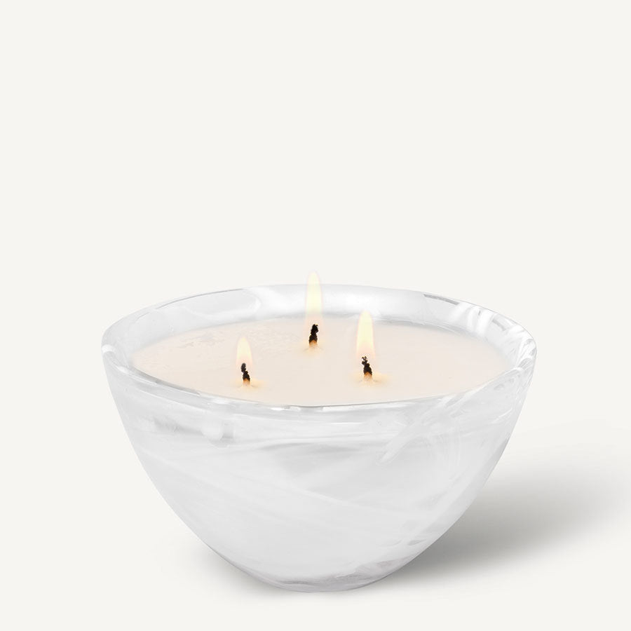 The KostaBoda Home Fragrance Collection features the Contrast White Candle in Woodland Vanilla scent. With three wicks, it rests in a round bowl with a white marble pattern, blending timeless elegance and warm glow reminiscent of Kosta Boda artistry.