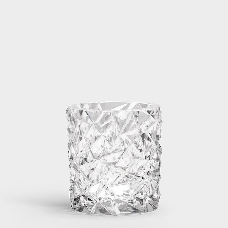 The Orrefors Carat Candle Holder Medium, with its faceted clear glass and textured geometric design, stands elegantly against a plain background, exuding timeless sophistication.