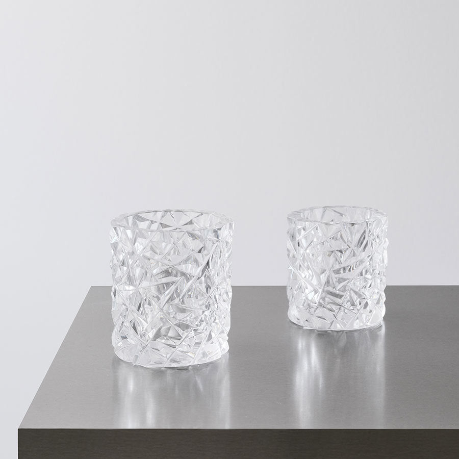 Two small Carat candle holders by Orrefors sit elegantly on a metallic surface against a plain background.