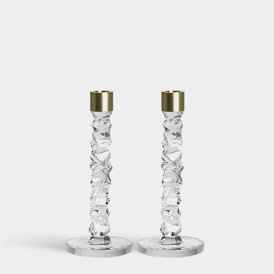 The Orrefors Carat Candlestick Brass Medium 2-Pack features two intricately designed clear candlesticks with gold-colored tops, stand elegantly on round bases against a plain white background.