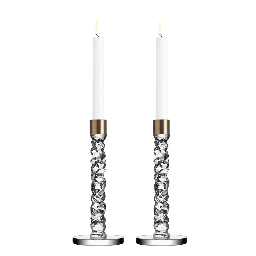 Two lit white candles are elegantly set in Orrefors Carat Candlesticks with twisted glass stems, in brass medium holders, standing proudly on round bases from the Orrefors: Carat Candlestick Brass Medium (2-Pack).