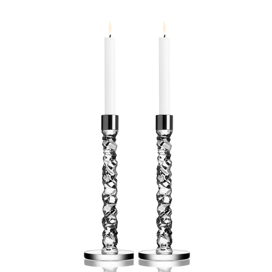 Two tall white candles stand in the elegant Orrefors Carat Candlestick Silver Large (2-Pack) against a plain white background.