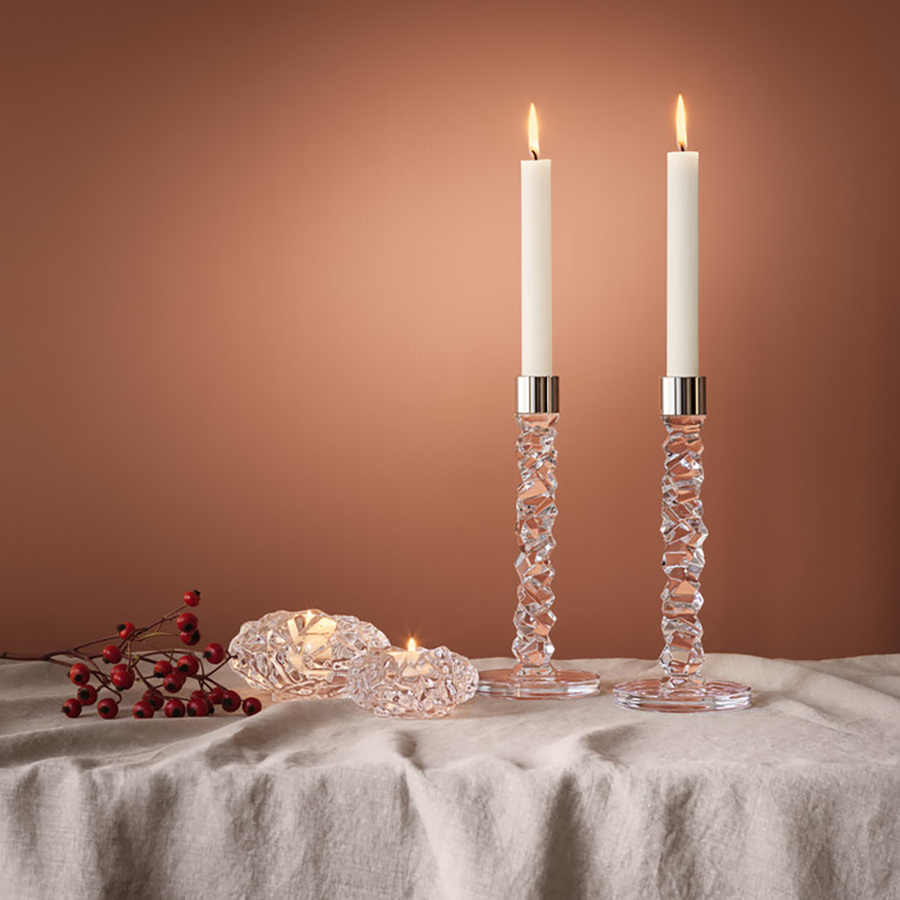 Two Orrefors Carat Candlestick Silver Large and two small votive candles rest on a textured cloth, accented by red berries against a warm brown background.