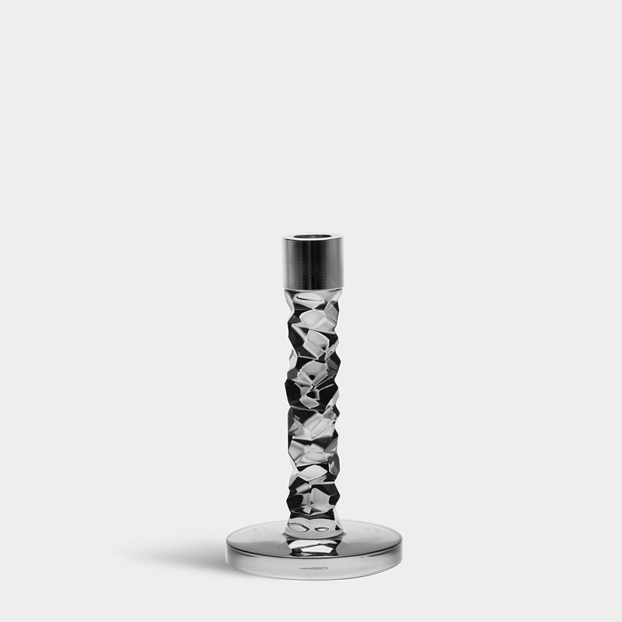 The Orrefors Carat Graphite Candlestick Small boasts a textured, faceted stem that elegantly gleams against a plain gray background.