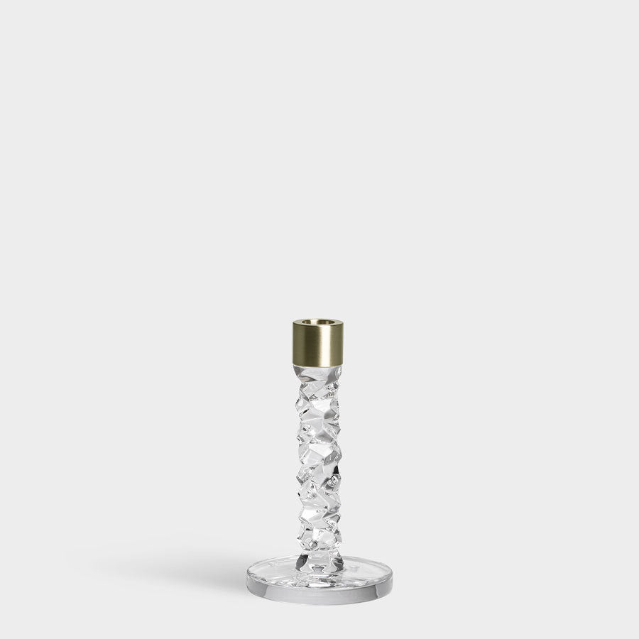 The Orrefors: Carat Candlestick Brass Small showcases a stunning crystal glass design with a gold-toned top, elegantly set against a gray background.