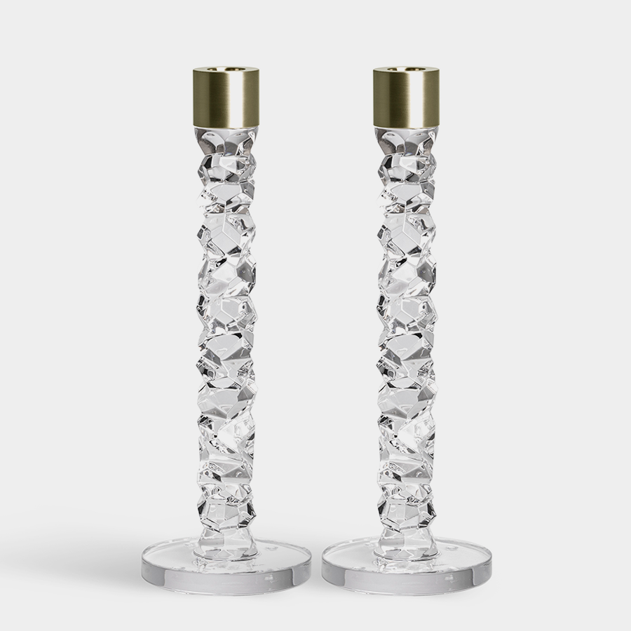 The Orrefors Carat Candlestick Brass Large (2-Pack) showcases textured crystal stems and gleaming brass holders, elegantly set against a plain backdrop.