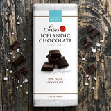 An Icelandic dark chocolate bar with sea salt on a wooden surface, broken pieces around it, and visible salt crystals scattered nearby.