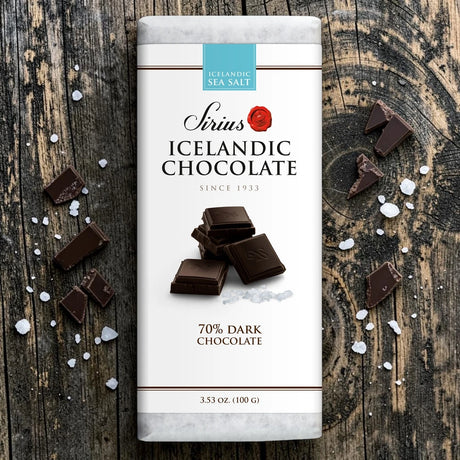 An Icelandic dark chocolate bar with sea salt on a wooden surface, broken pieces around it, and visible salt crystals scattered nearby.