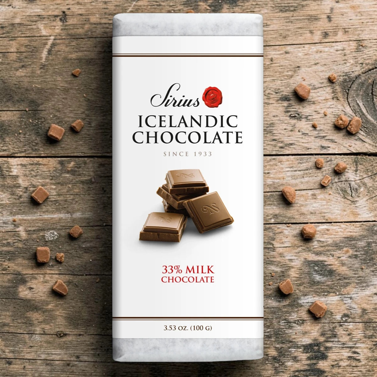 Sirius chocolate bar labeled 33% cocoa on a wooden surface with several pieces of broken Icelandic milk chocolate around it.