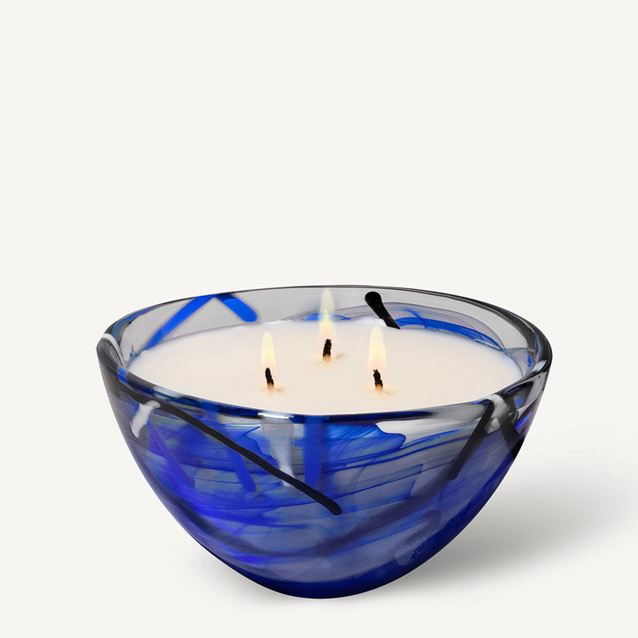 The KostaBoda: Contrast Candle Blue is a blue and clear glass bowl-shaped holder with abstract black lines around a lit three-wick white candle, capturing coastal bloom and enhancing your home fragrance experience.