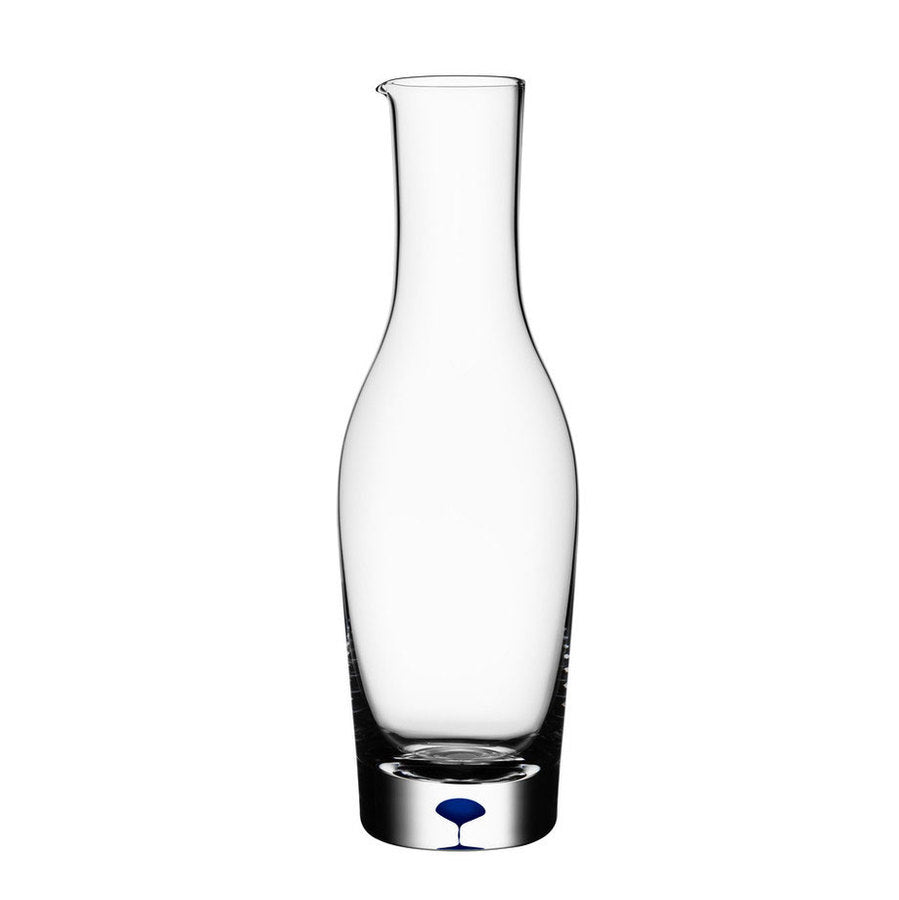 The Orrefors Intermezzo Blue Carafe by Erika Lagerbielke features a clear glass design, narrow neck, and distinctive blue droplet at the base; it holds 37 oz.