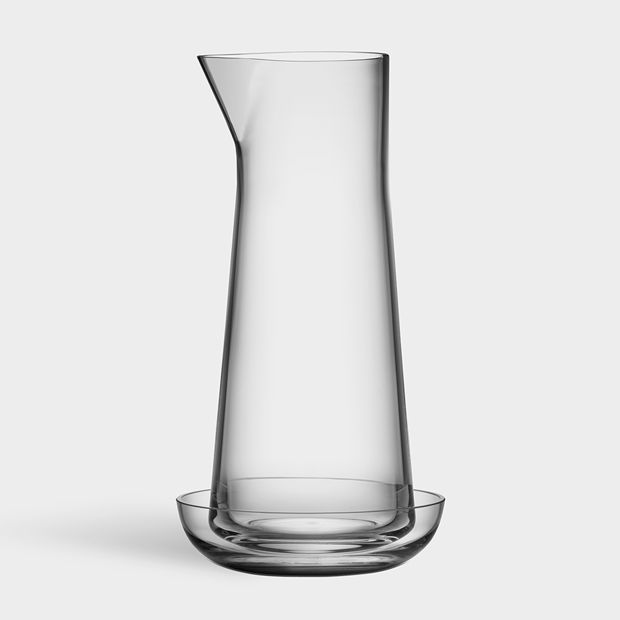 The Orrefors Informal Clear Carafe with Bowl, designed by Björn Dahlström, stands elegantly with its tall narrow neck, resting gracefully in a small glass bowl on a pristine white background.